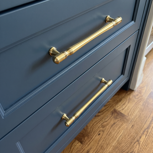 Brass cabinet handles on navy blue drawers with wooden flooring