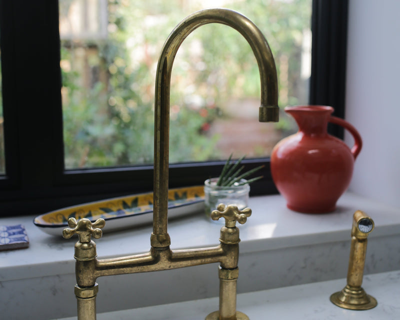 Brass kitchen faucet on a marble countertop with a window in the background